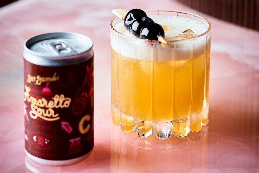 An amaretto sour with olive decoration and a can of the Italian premixed drink.