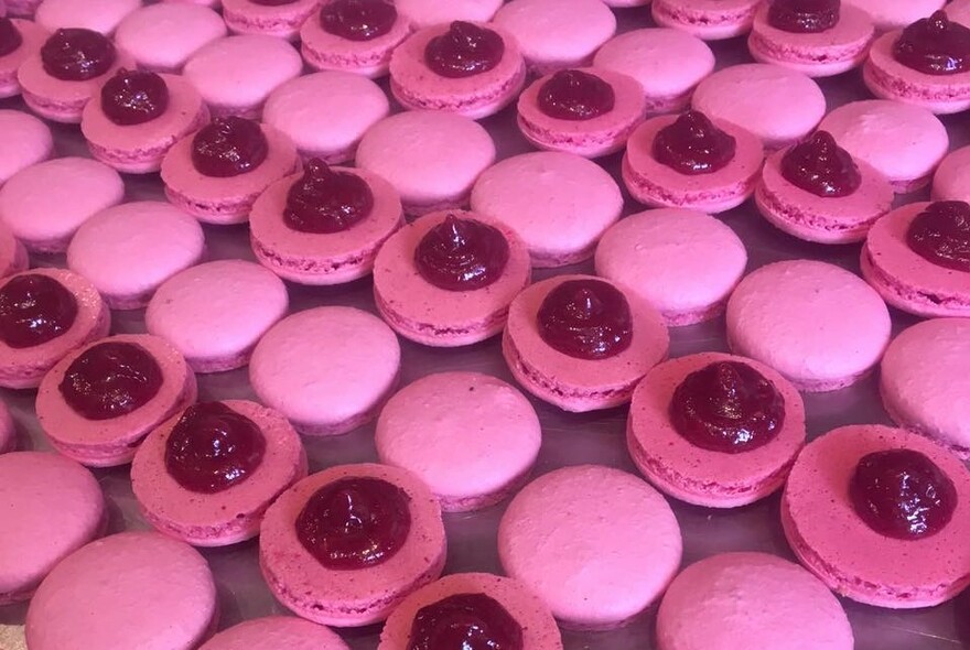 A tray of pink macarons, some topped with red cream.