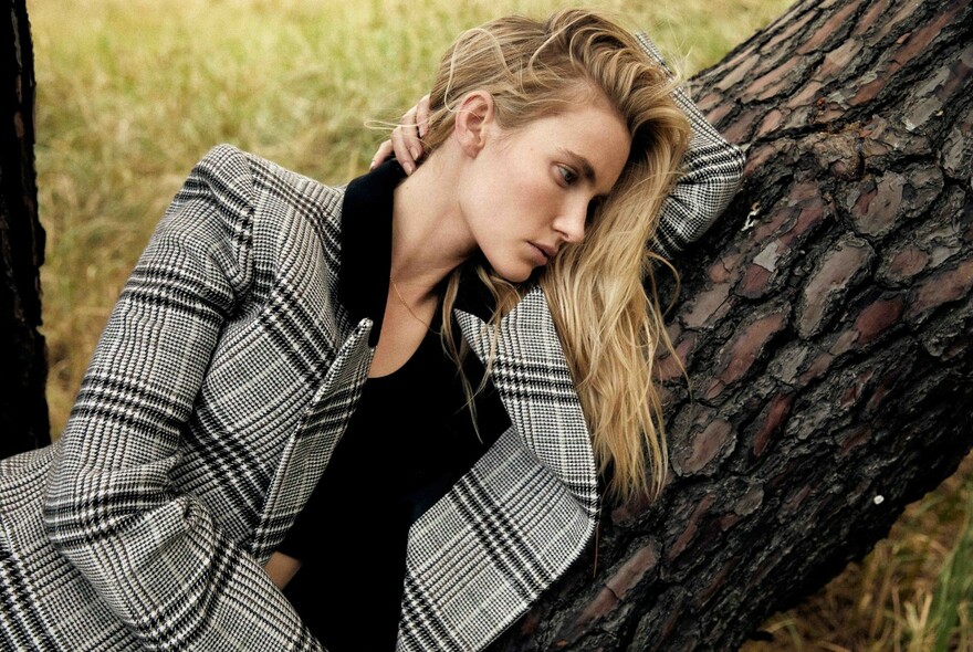 Model wearing a plaid jacket and black shirt, leaning against a tree.