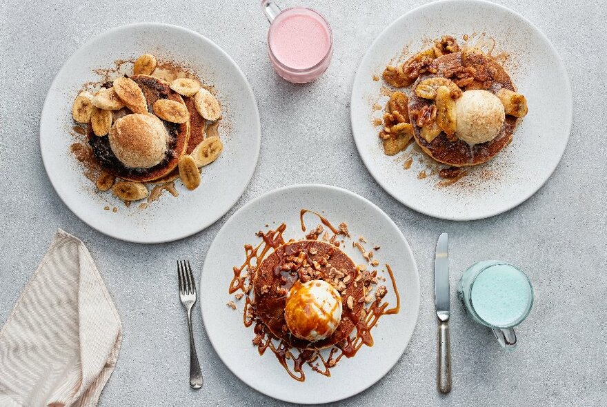 Looking down on three plates of pancakes, all with a scoop of ice cream and various toppings. 