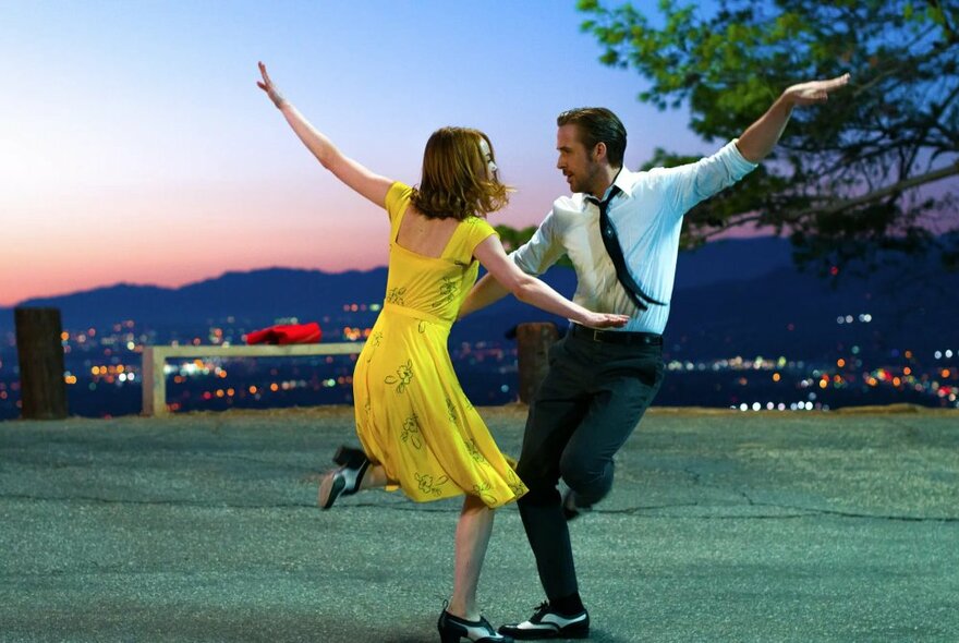 Ryan Gosling and Emma Stone dancing with LA lights in the background in a still from the film La La Land.