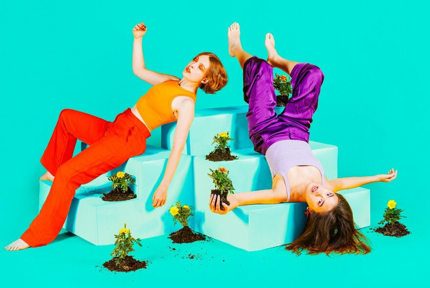 Two people seated on step props with plants, one person seated upside down.