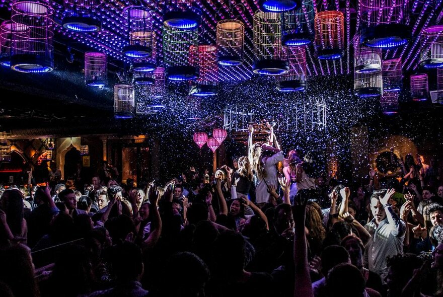 Inside a packed nightclub with people dancing under an illuminated ceiling. 