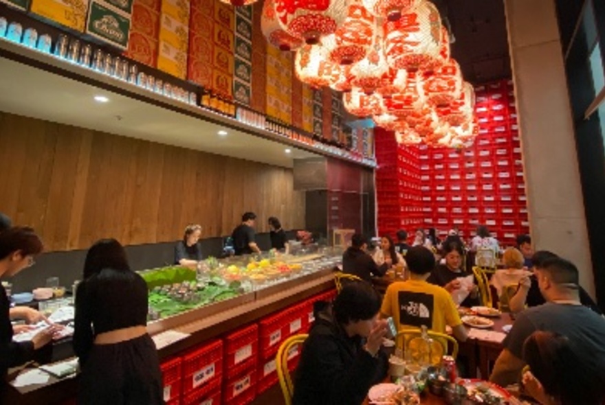 A crowded Thai eatery with tables close to a display of food. 