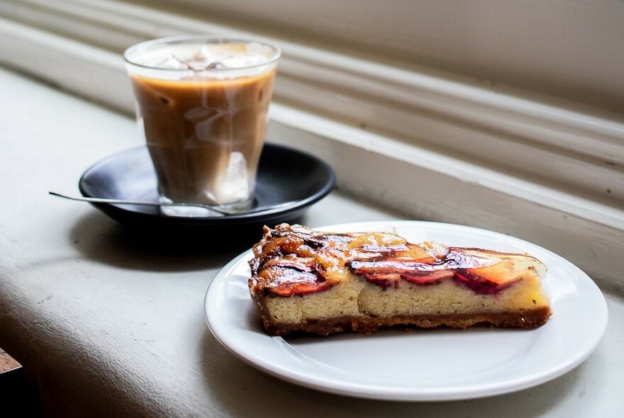 Glass of coffee with a slice of fruit flan.