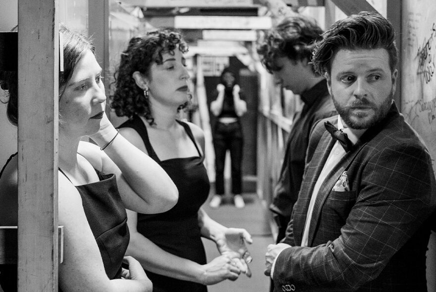 Black and white shot of four performers backstage, waiting to go on stage.