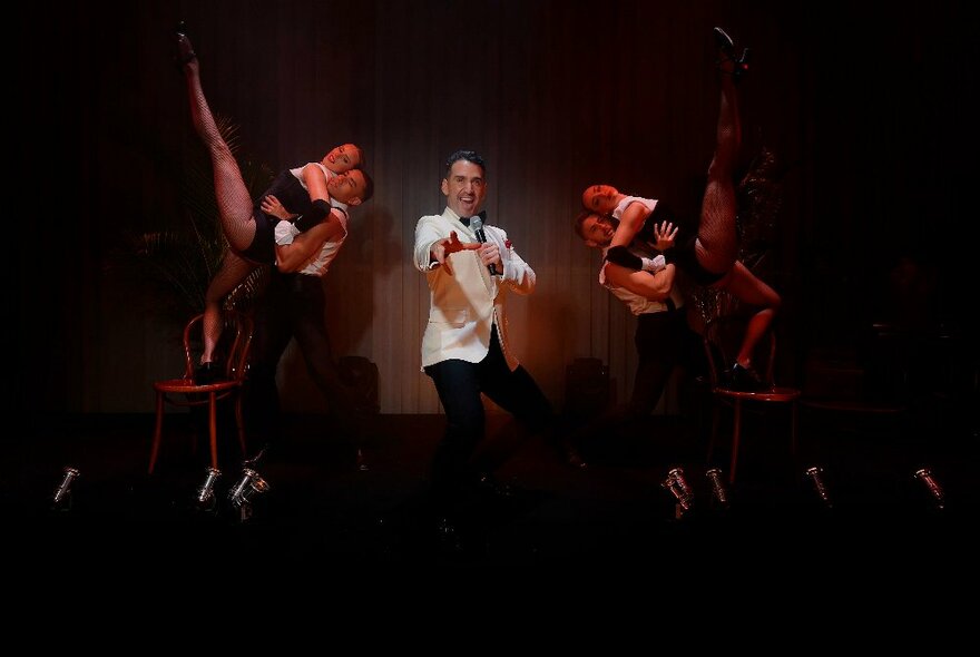 Performer, Mike Snell, singing on stage in a white tuxedo, with cabaret dancers on either side.