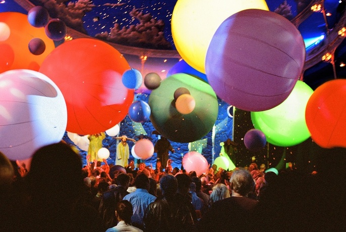 Huge balloons float above an audience in a theatre.