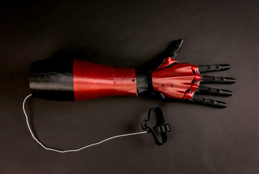 A bionic arm made from red and black steel, with a cord and handle attached.