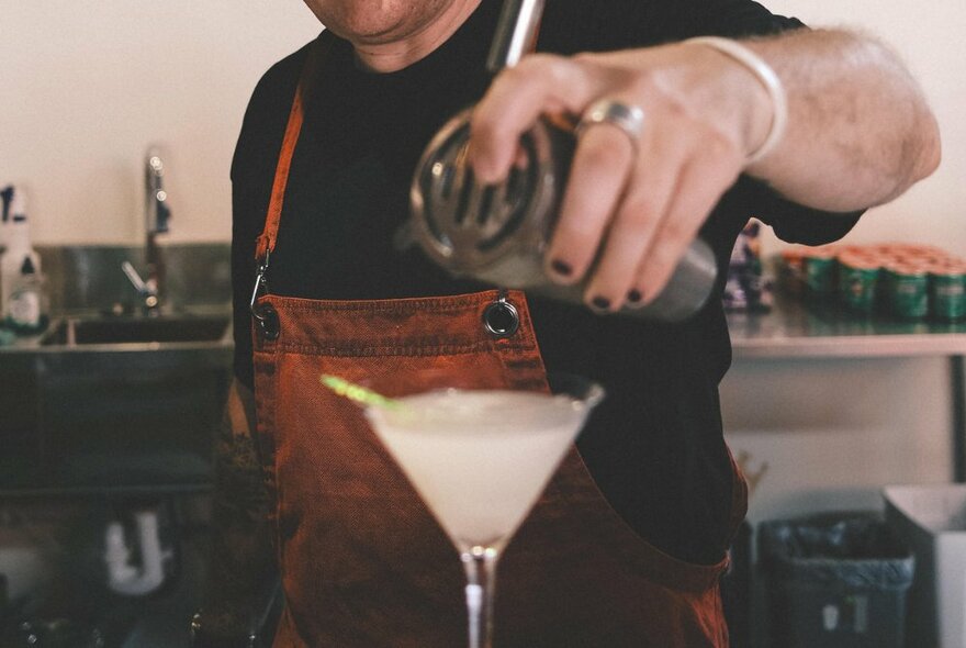 Bartender pouring a cocktail from a shaker into a martini glass.