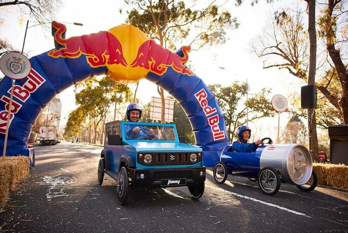 A billy cart race with a blue car cart and a red bull can cart.