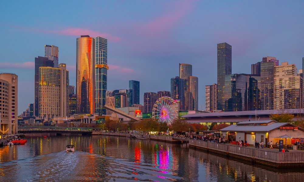 A view of a river at sunset with a Ferris wheel and a city skyline in the background.