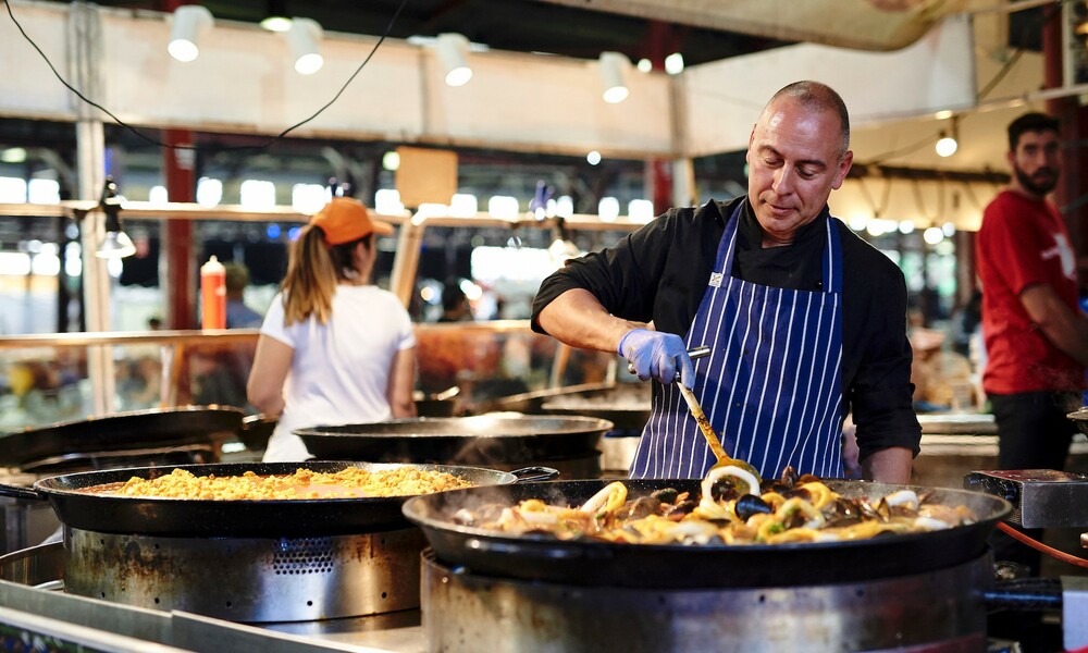 Chef standing over a large group of paella pans, stirring the food.