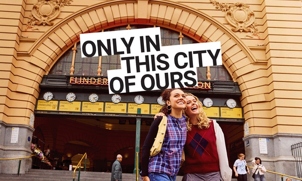 Two women laughing arm-in-arm in front of Flinders' street station