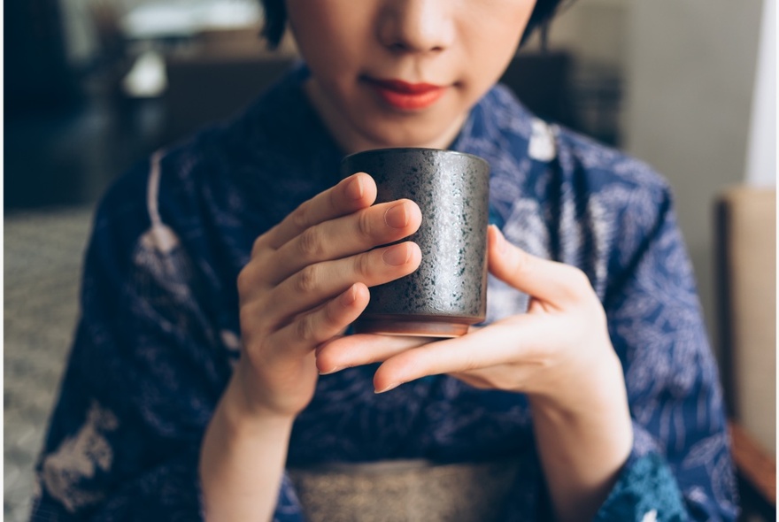 A Japanese woman wearing a traditional kimono and gently holding a cup of Japanese tea.