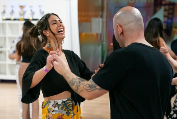 A couple facing each other and holding hands dancing in a dance studio, the woman laughing.