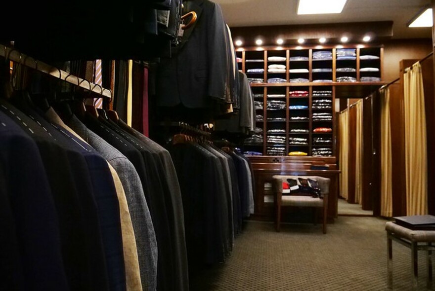 Row of suits and shelves with folded clothing in the background.