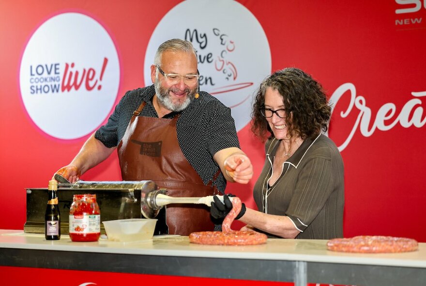 Two people on stage making sausages at a cooking demonstration.