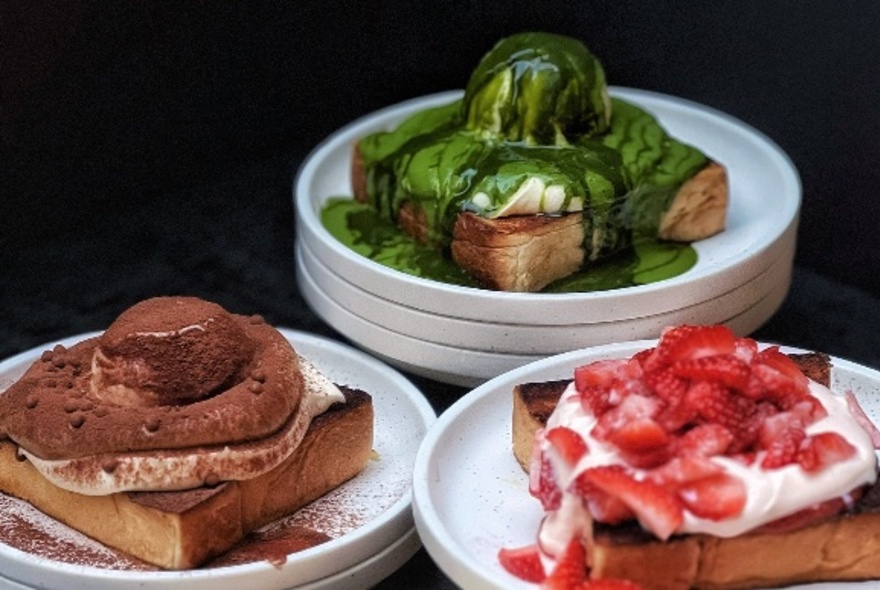White plates with desserts including toast topped with chocolate, green matcha syrup, cream and strawberries.