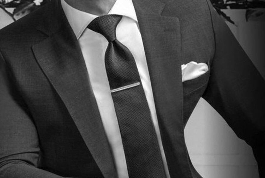 Black and white image of suit jacket, kerchief, tie with tie pin, and shirt.