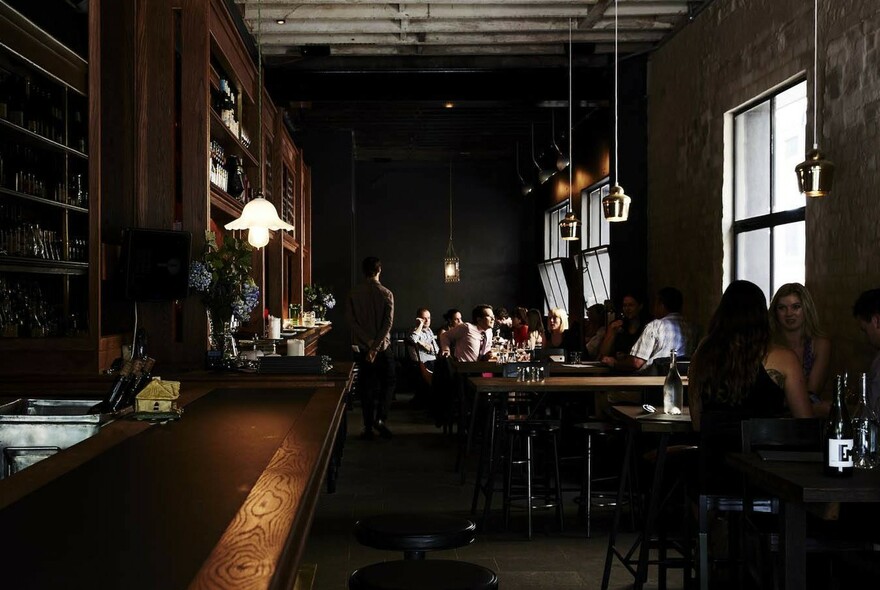 Dimly lit wine bar with people seated at small dark tables.