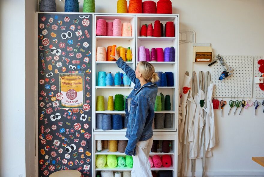 A woman browsing a wall of colourful yarn.