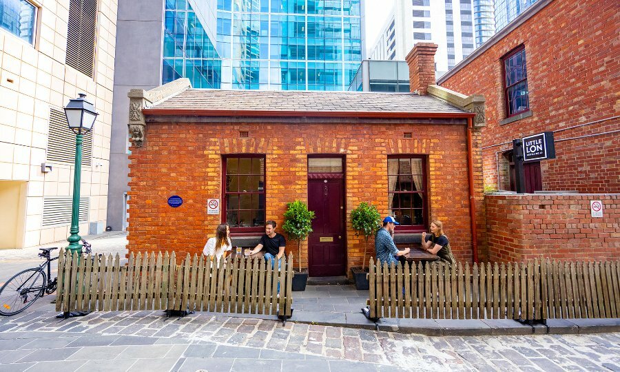 Four people dining outside a tiny brick venue with a picket fence. 