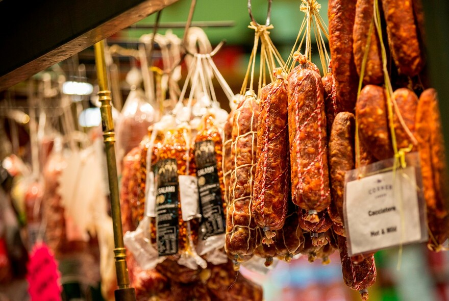 Salami and other cured meats hanging by string on hooks.