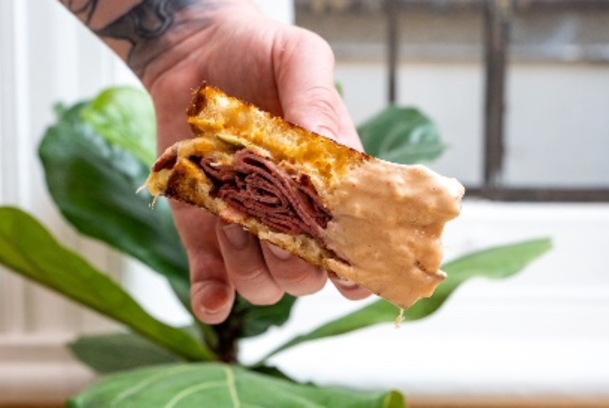 A hand holding a pastrami toastie.