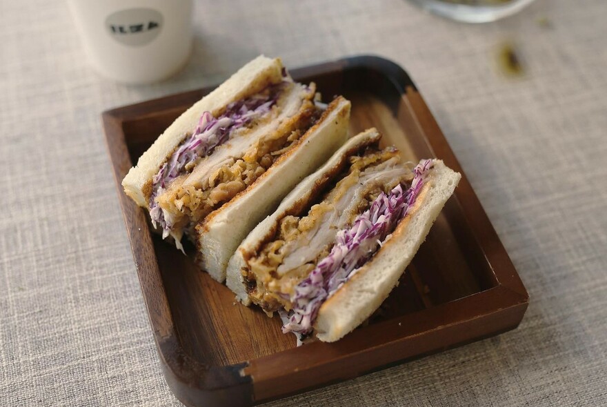 Chicken katsu sandwiches with coleslaw on a wooden platter.