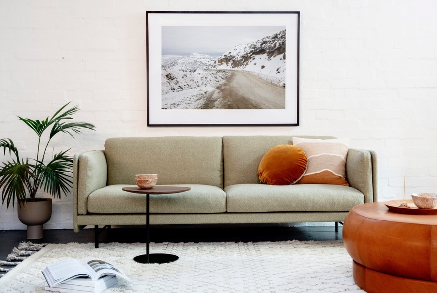 Room with a modern couch, pillows, small coffee table, a white rug, potted plant and artwork hanging on the wall. 