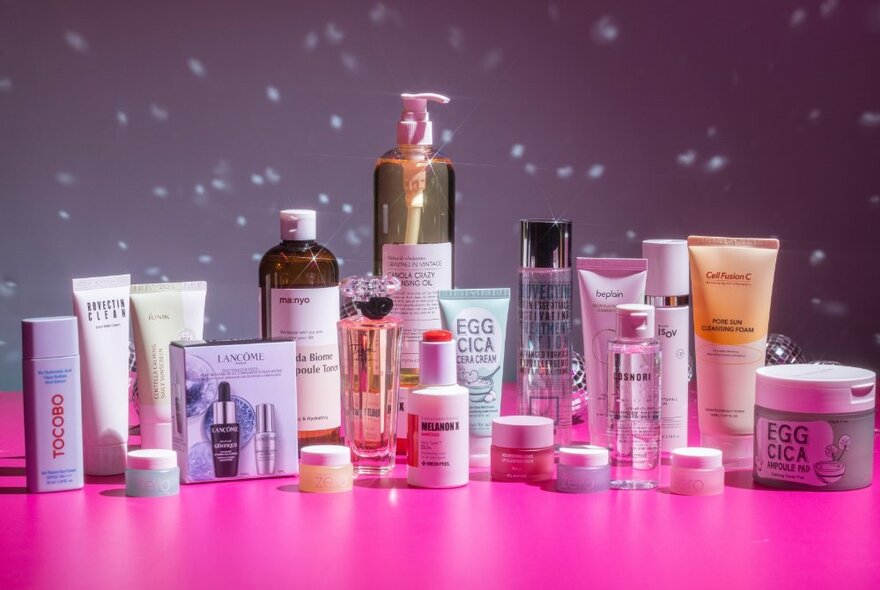 A range of skincare and cosmetics arranged on a pink table 