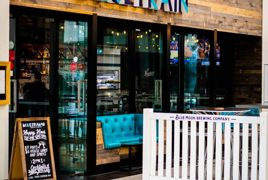 Exterior of Bluetrain restaurant at Southbank, large glass doors open to show a glimpse of booth seating inside, and a chalkboard of specials.