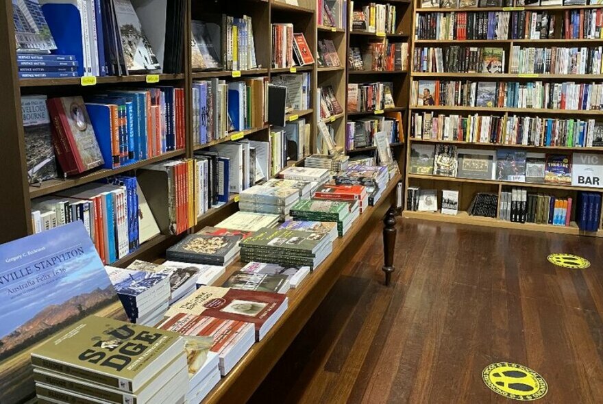 Interior of a bookstore with shelves and tables with piles of books for sale.