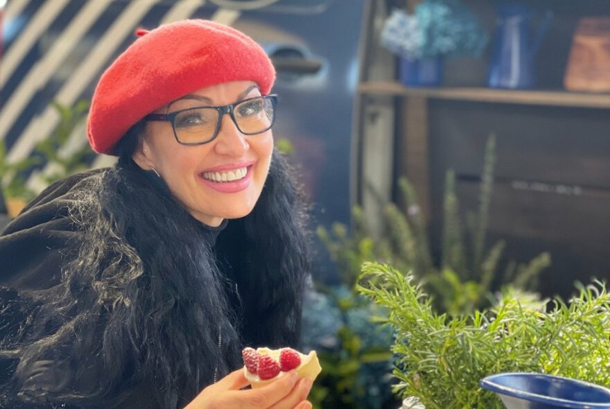 A woman wearing a red beret and black glasses, eating a French pastry.