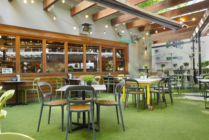 The interior of an empty bar with green floors resembling grass, and casual chairs and tables