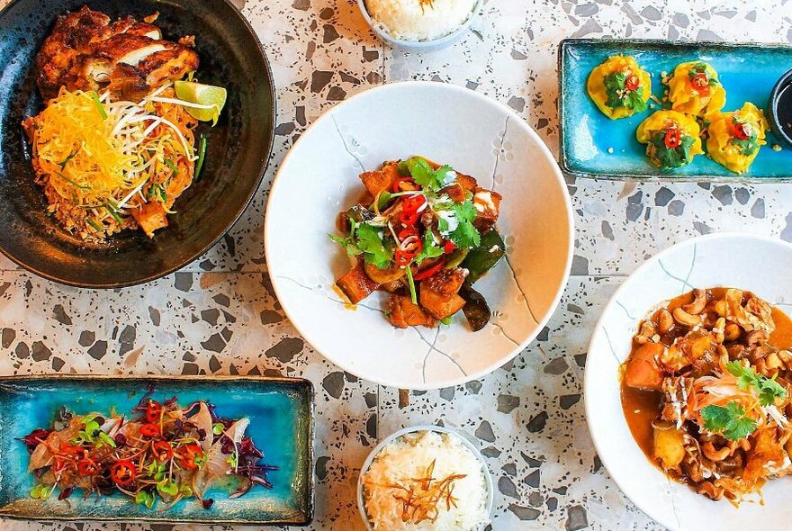 Several dishes of Thai food on a grey terrazzo table.