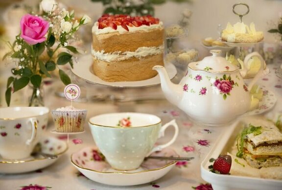 High tea spread with floral crockery, tiered strawberry cream cake and flowers.