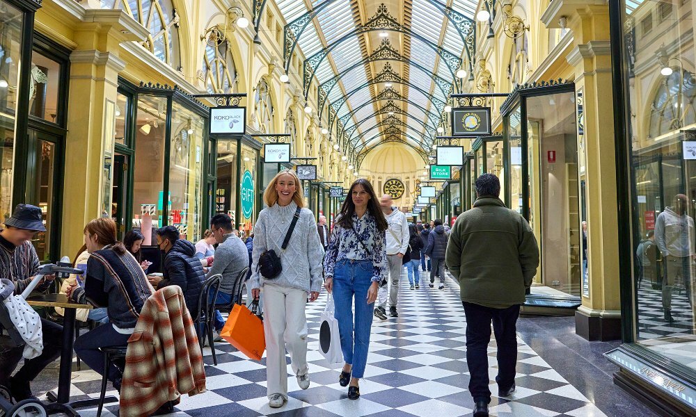Two women walking through a busy shopping arcade with shopping bags.