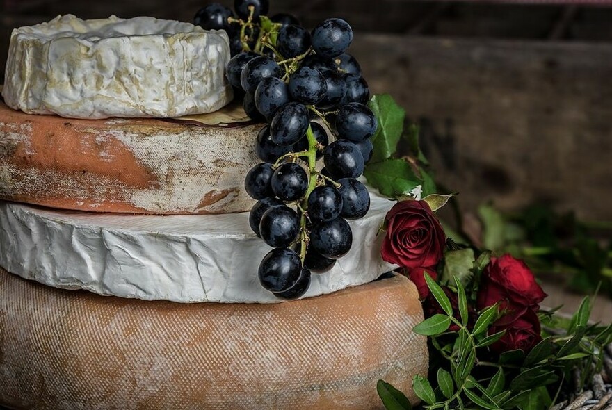 A stack of large and small whole cheeses and a bunch of grapes.