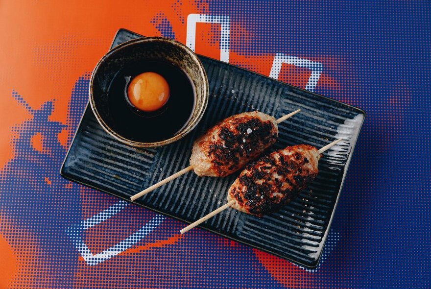 Japanese dish with meat on skewers and a bowl with an egg yolk in it.