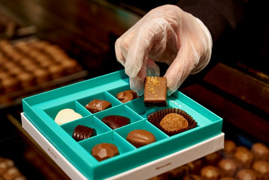 Someone taking a chocolate from a teal assorted box.