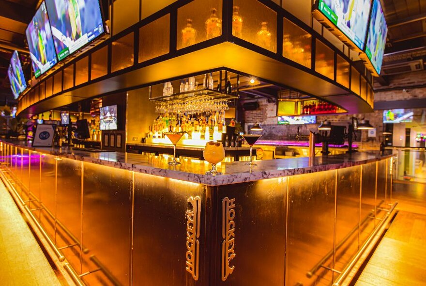 Golden-lit bar, seen from corner, with screens along top.