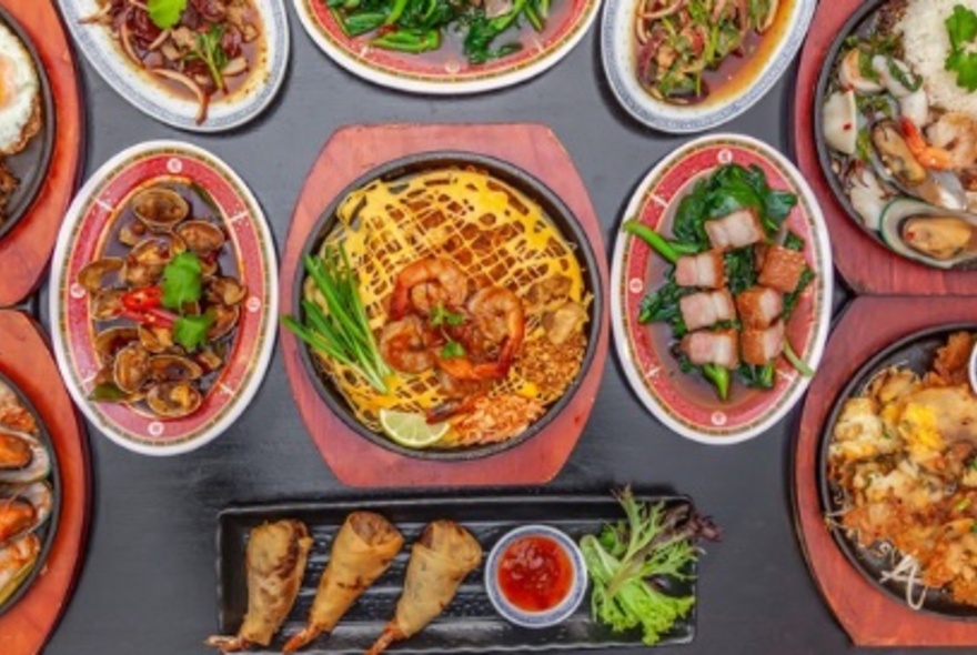 An array of Thai dishes and platters on a grey table.