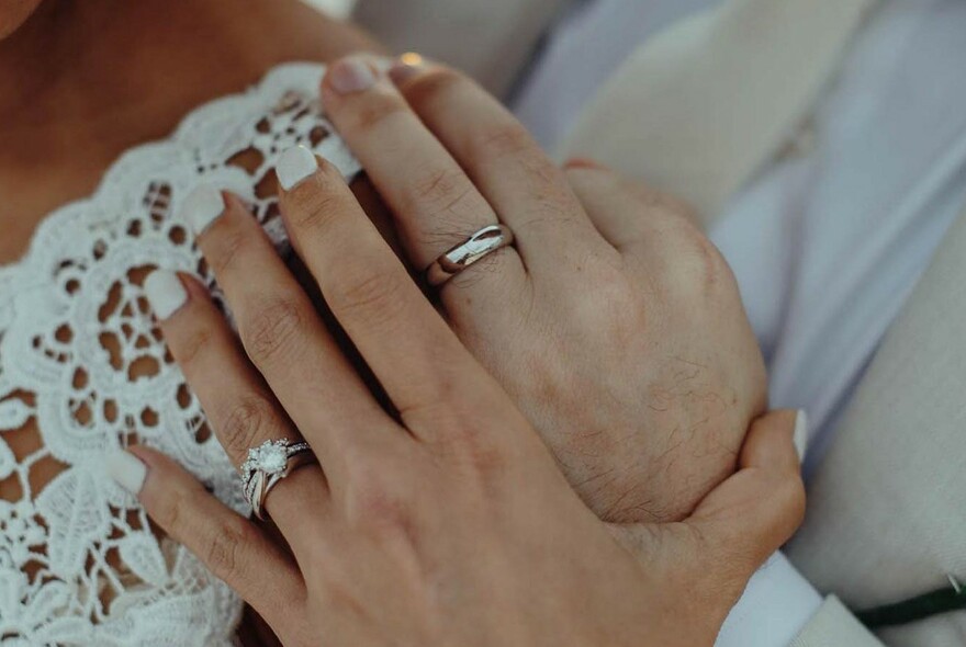 Male and female hands with wedding bands and diamond engagement ring.