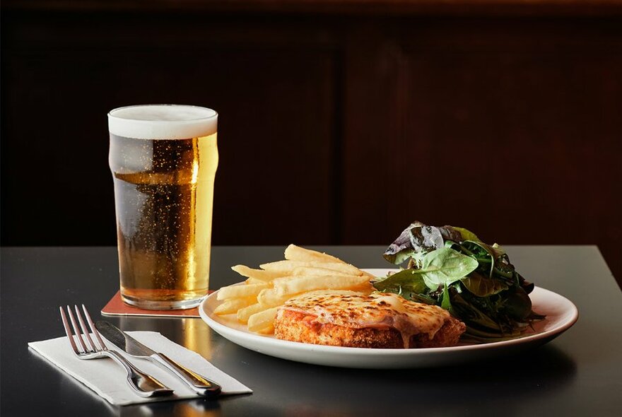 A chicken parma, chips and salad on a plate, with a glass of beer alongside.