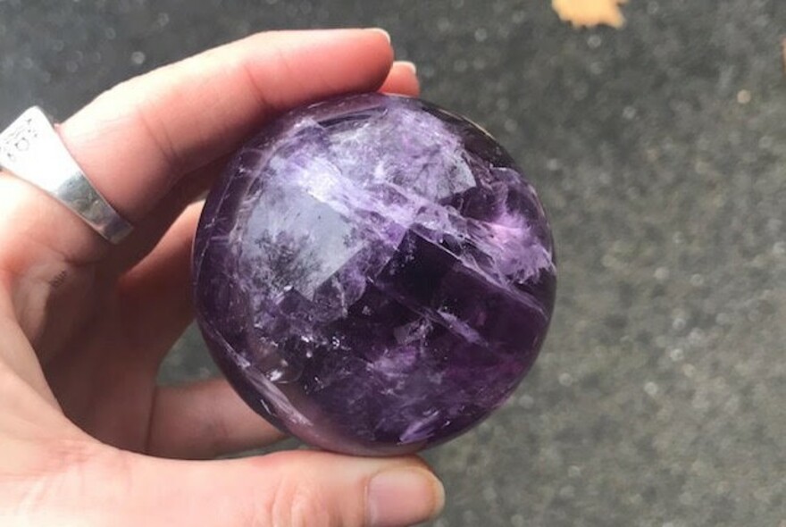Hand with sliver ring holding a large round purple crystal.