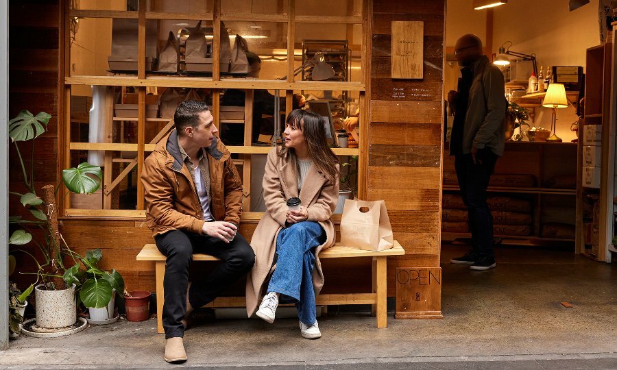 A couple drinking coffee outside a small bakery with timber walls.