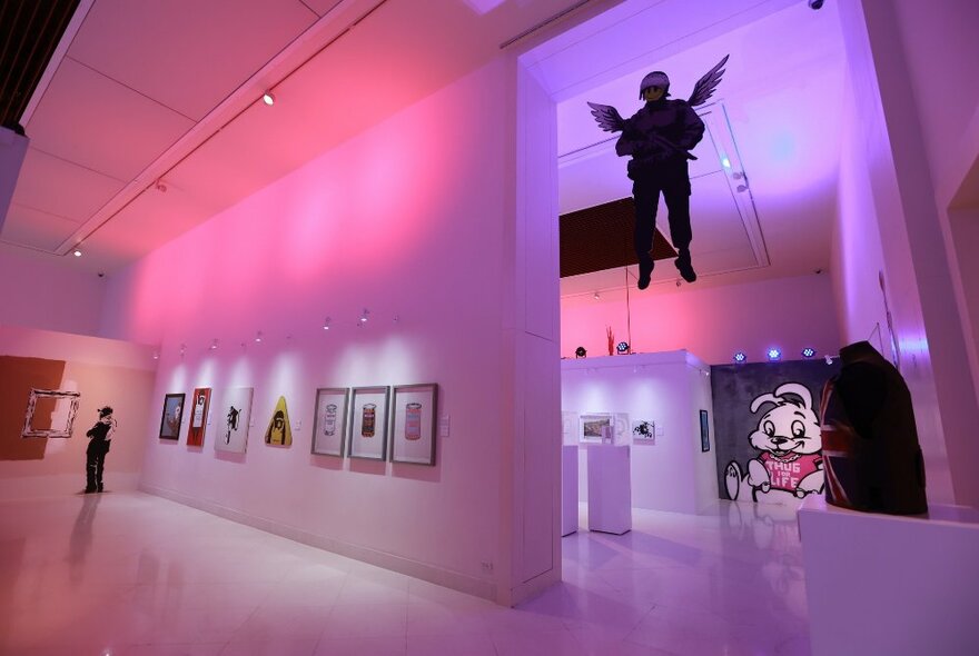 Banksy artworks displayed in a gallery with pink lights. 