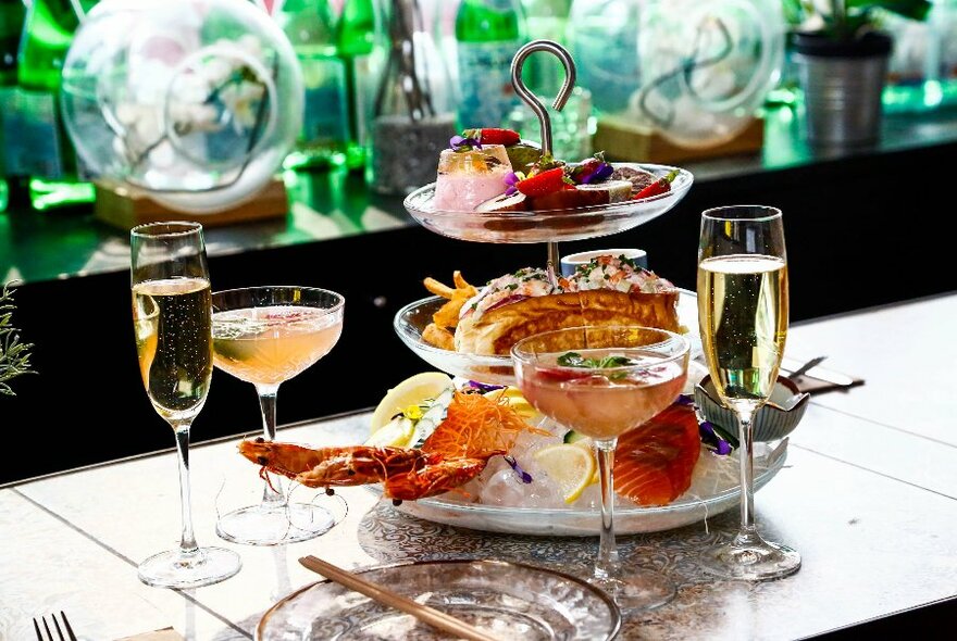 A tiered stand with lobster and more, with glasses of champagne and cocktails.